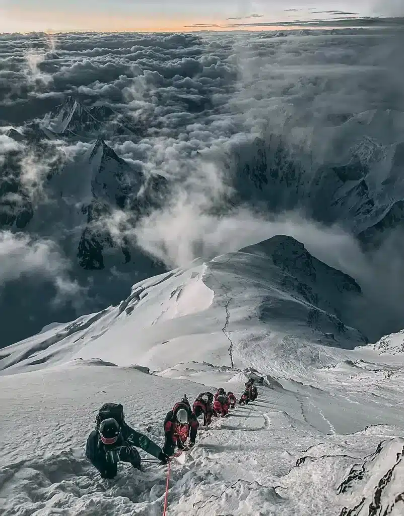 A diagram of the climbing route to the summit of K2, highlighting the "Bottleneck" couloir at 25,800 ft, located beneath a massive ice overhang. The path shows the technical traverse and the final ascent to the summit at 28,251 ft.